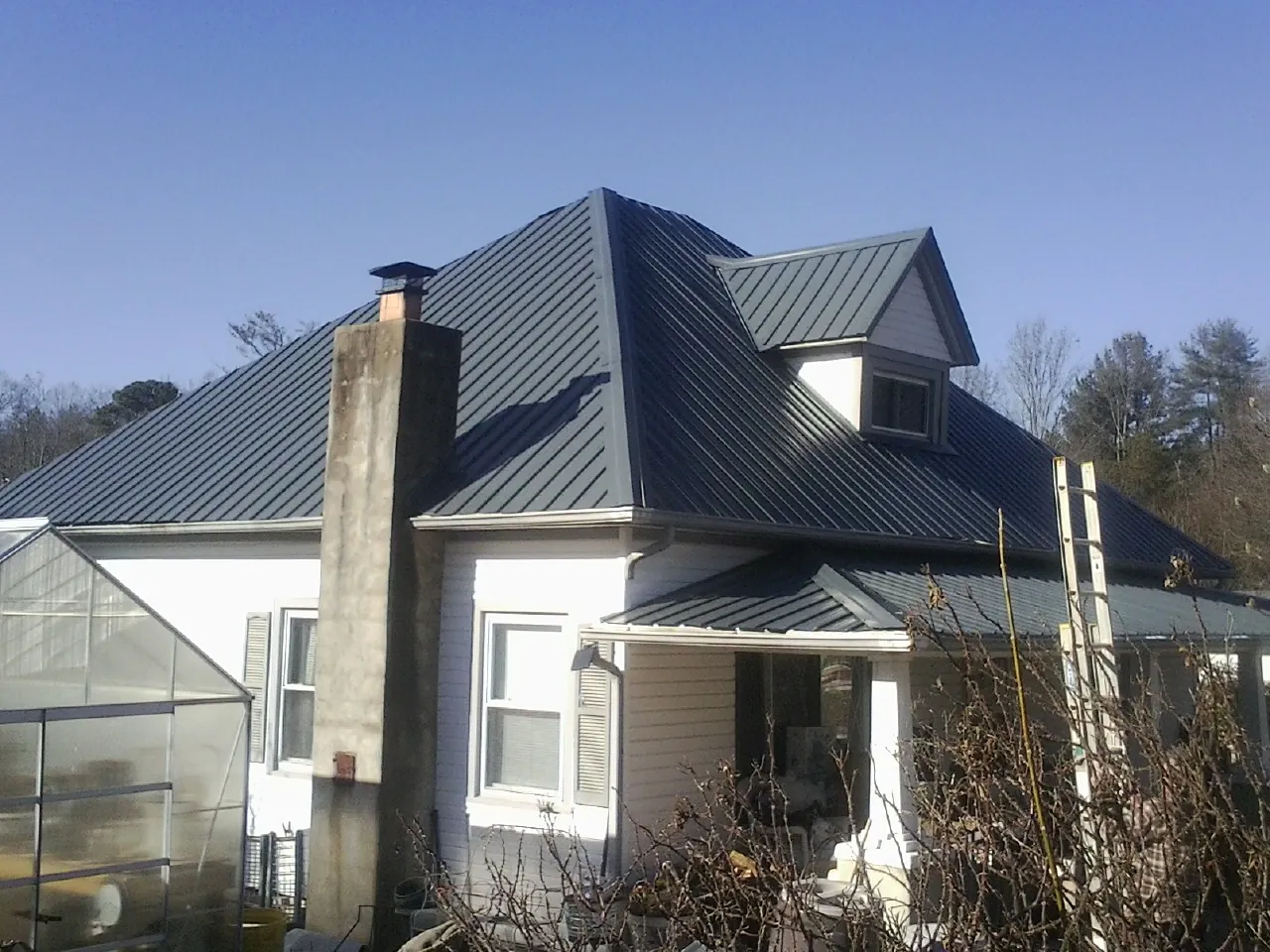 Dark blue standing seam metal roof on a white farmhouse with dormer — Slate & Tile Roof Repair by Roofing Brothers in Pacific Grove