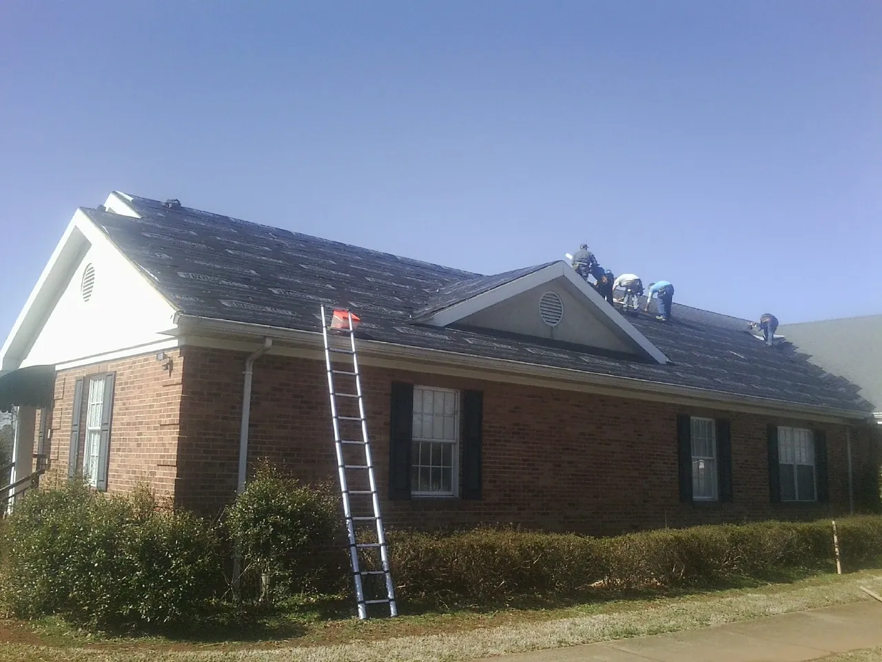 Crew tearing shingles off a brick ranch roof with a ladder set — Emergency Roof Repair work by our crew in Pacific Grove