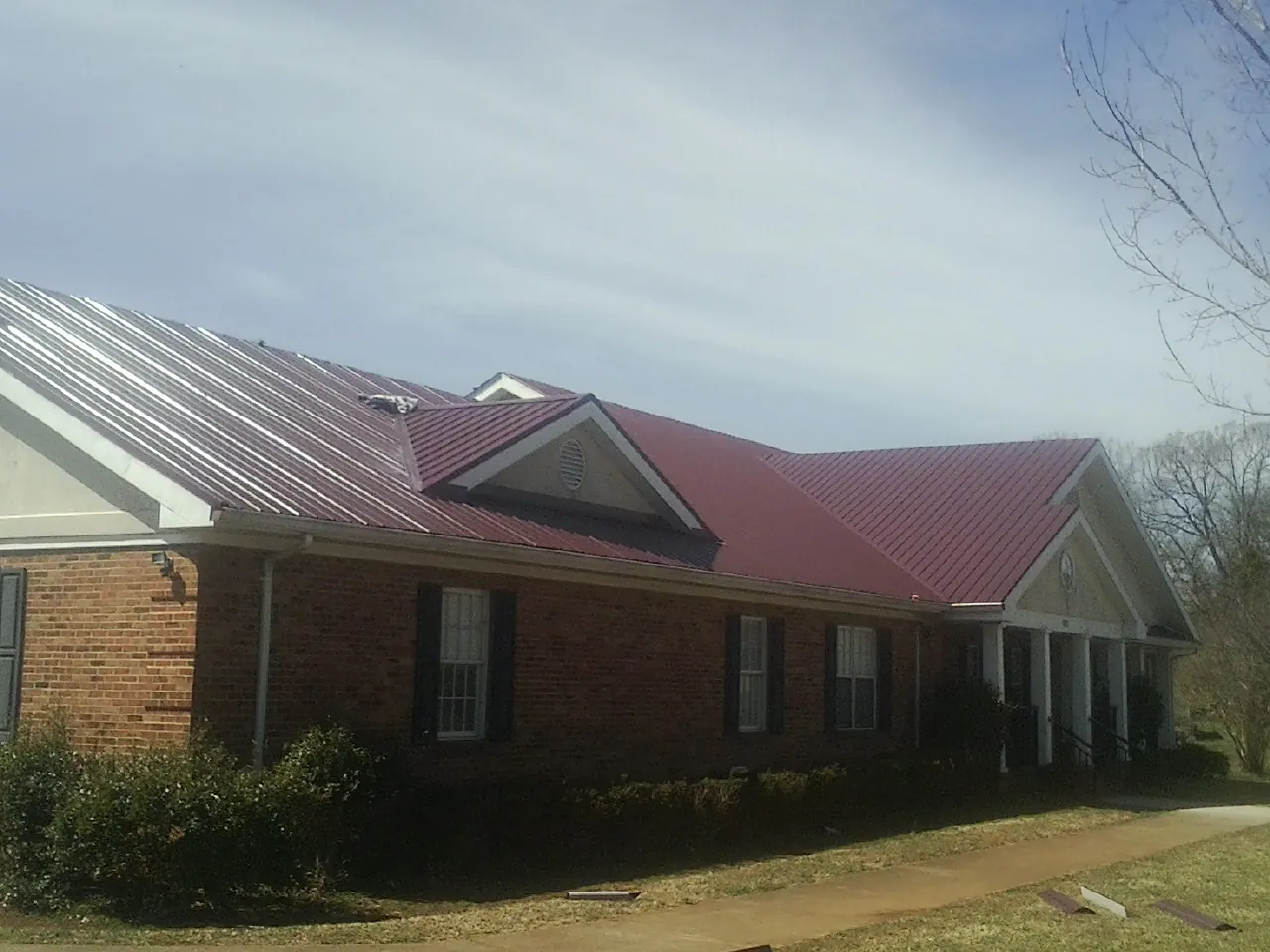 Red metal roof with gabled entries on a long brick building, from a Hail Damage Roof Repair job in Pacific Grove
