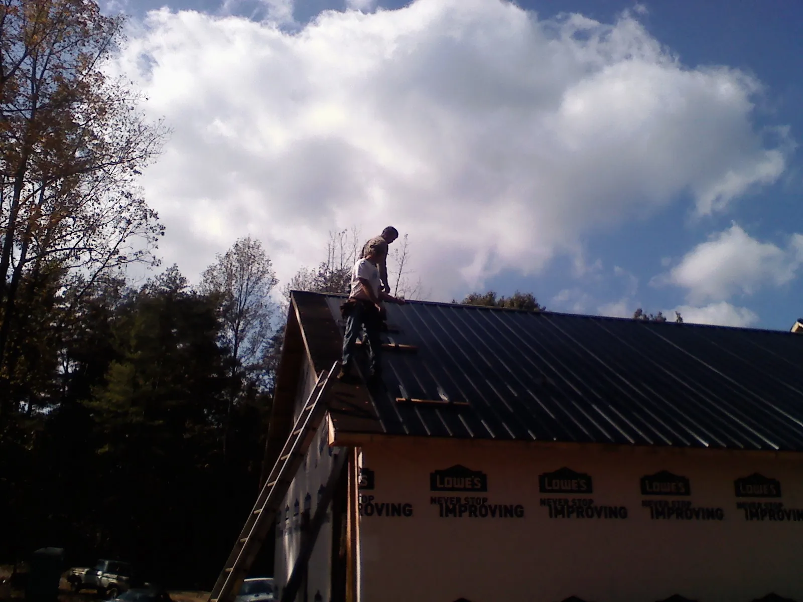 Roofer fastening dark metal panels high against a cloudy sky, from a Roof Inspection job in Pacific Grove