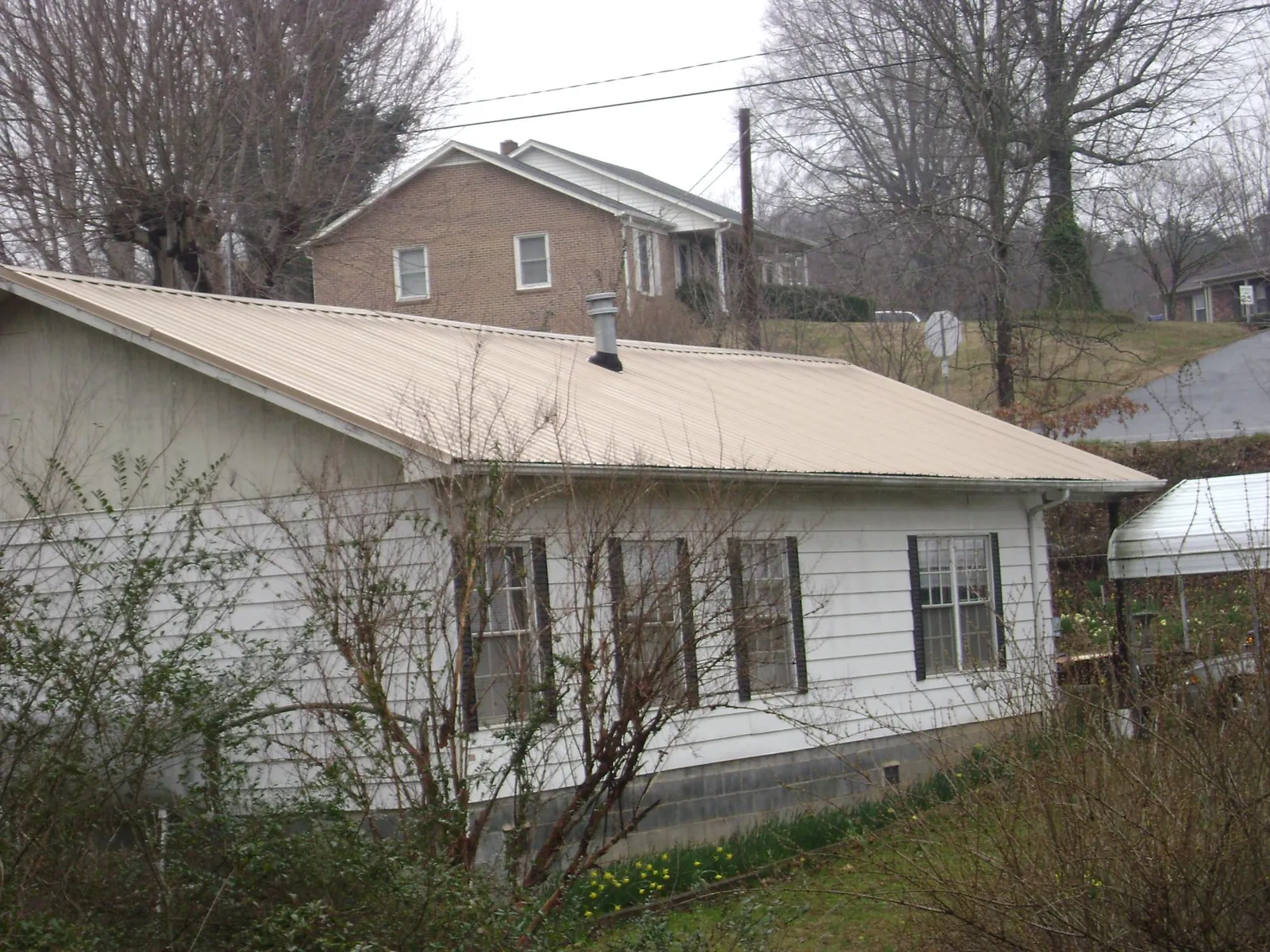 Tan metal roof on a white sided house set into a hillside — Commercial Roofing by Roofing Brothers in Pacific Grove